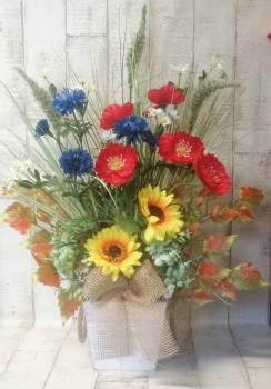 Dekoratives Sommergesteck im Mohnblume, Magerite, Kornblume im Holztopf